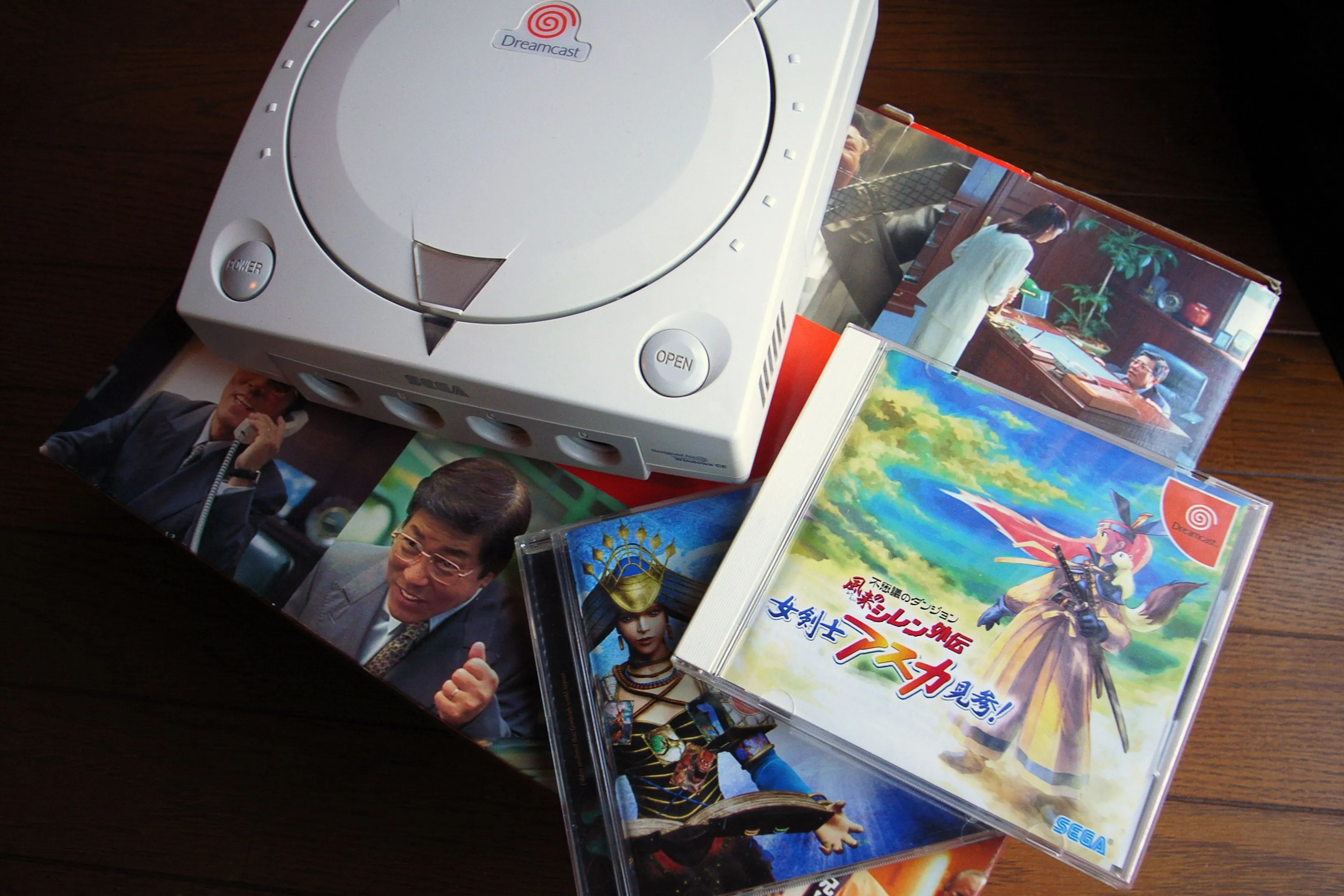 Bàn điều khiển Sega Dreamcast màu trắng đặt cùng một số đĩa game, thể hiện thiết kế đặc trưng và bộ sưu tập trò chơi