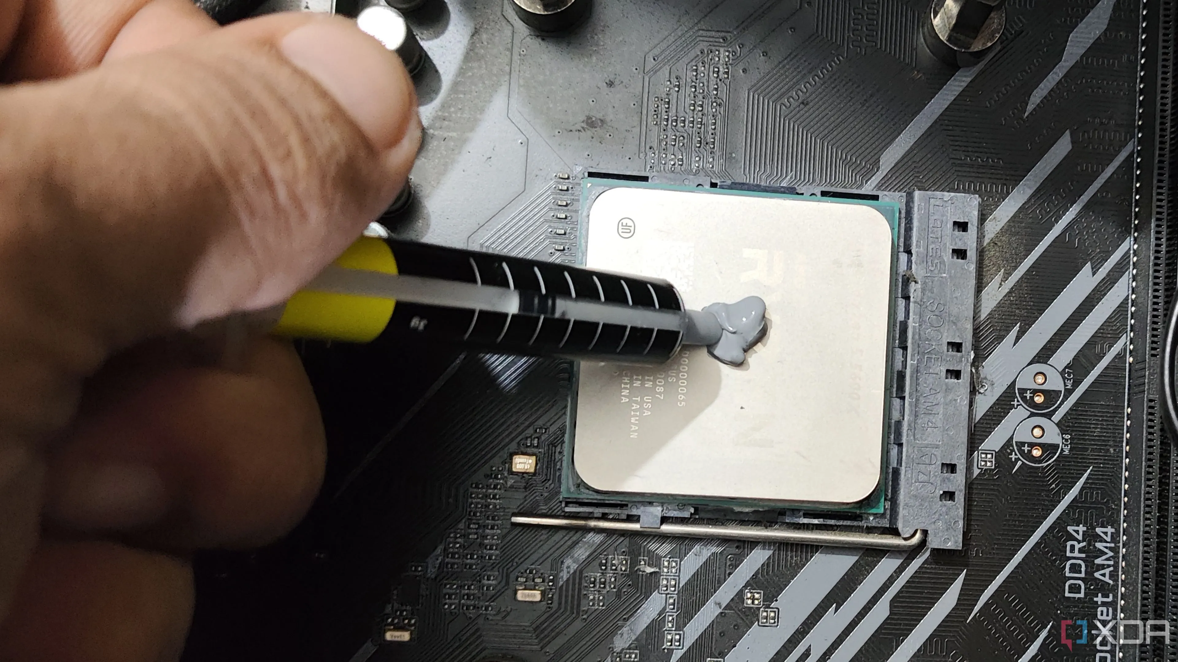 Hình ảnh một người đang bôi keo tản nhiệt lên bộ vi xử lý Ryzen 5 5600X, quy trình quan trọng giúp CPU và GPU hoạt động mát mẻ, duy trì hiệu suất ổn định khi chơi game.