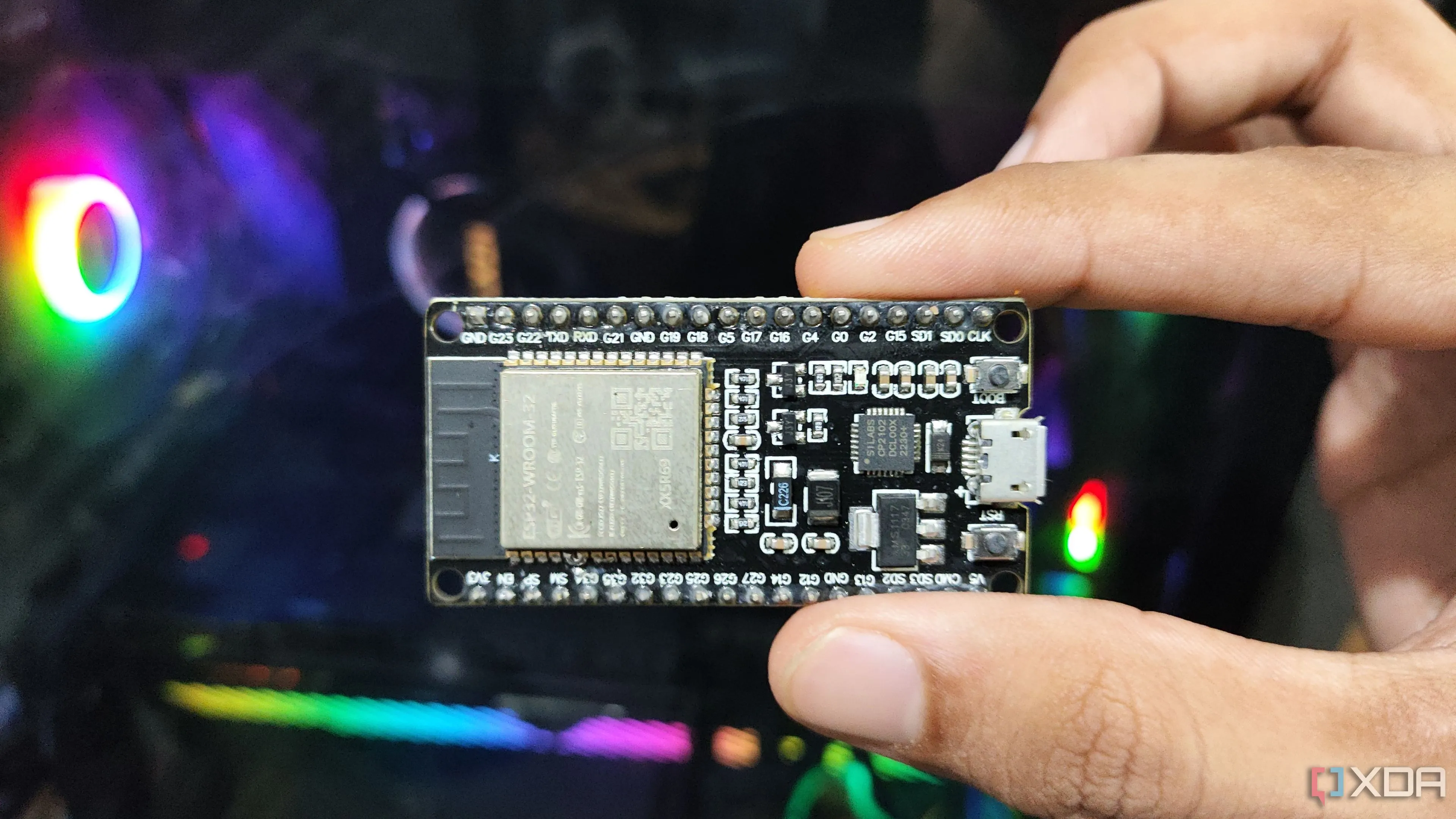 Hình ảnh một người đang cầm module vi điều khiển ESP32-WROOM-32 trước màn hình máy tính