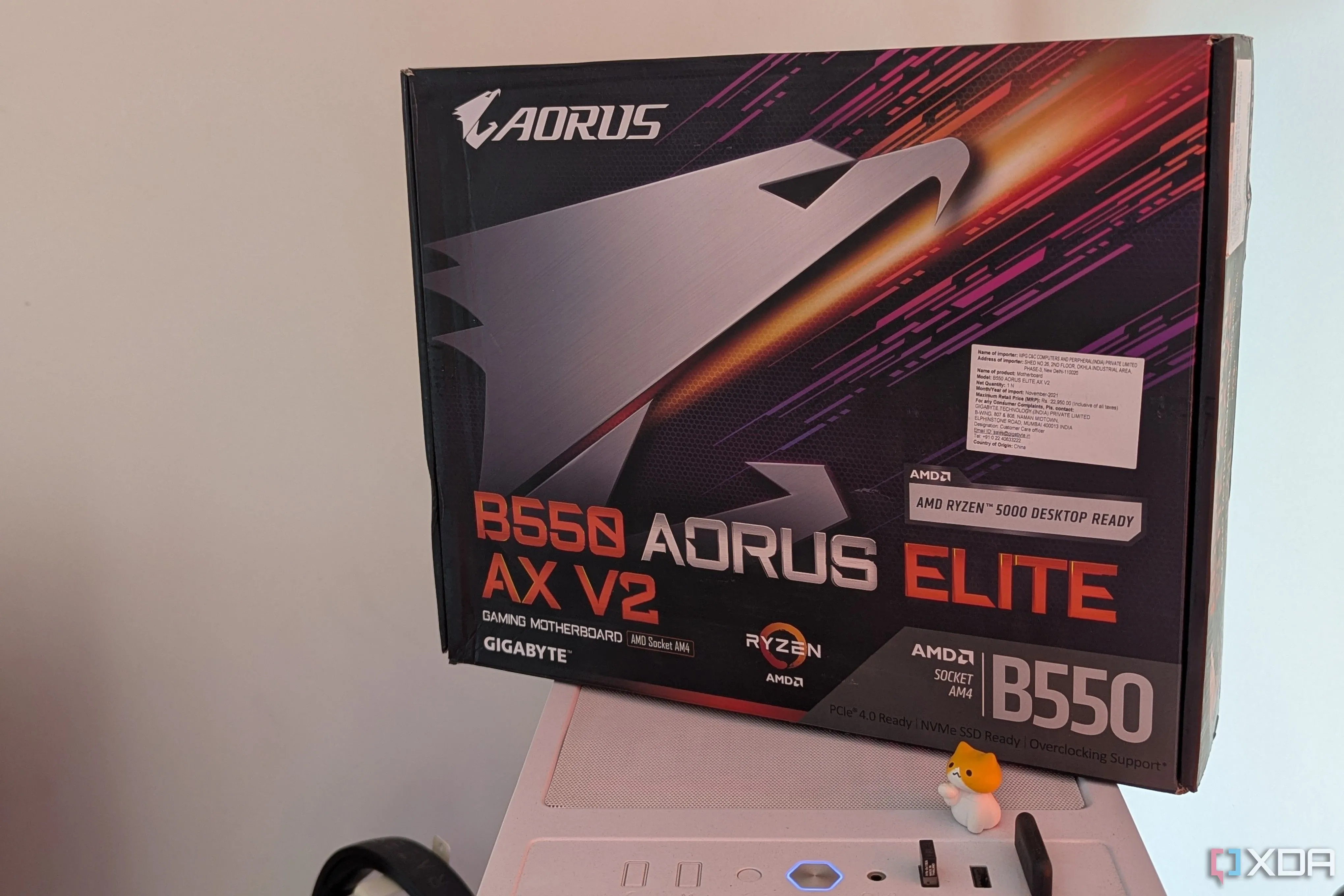 Hộp bo mạch chủ Gigabyte B550 Aorus Elite AX V2 đặt trên vỏ case máy tính màu trắng, đại diện cho mainboard có đèn RGB.