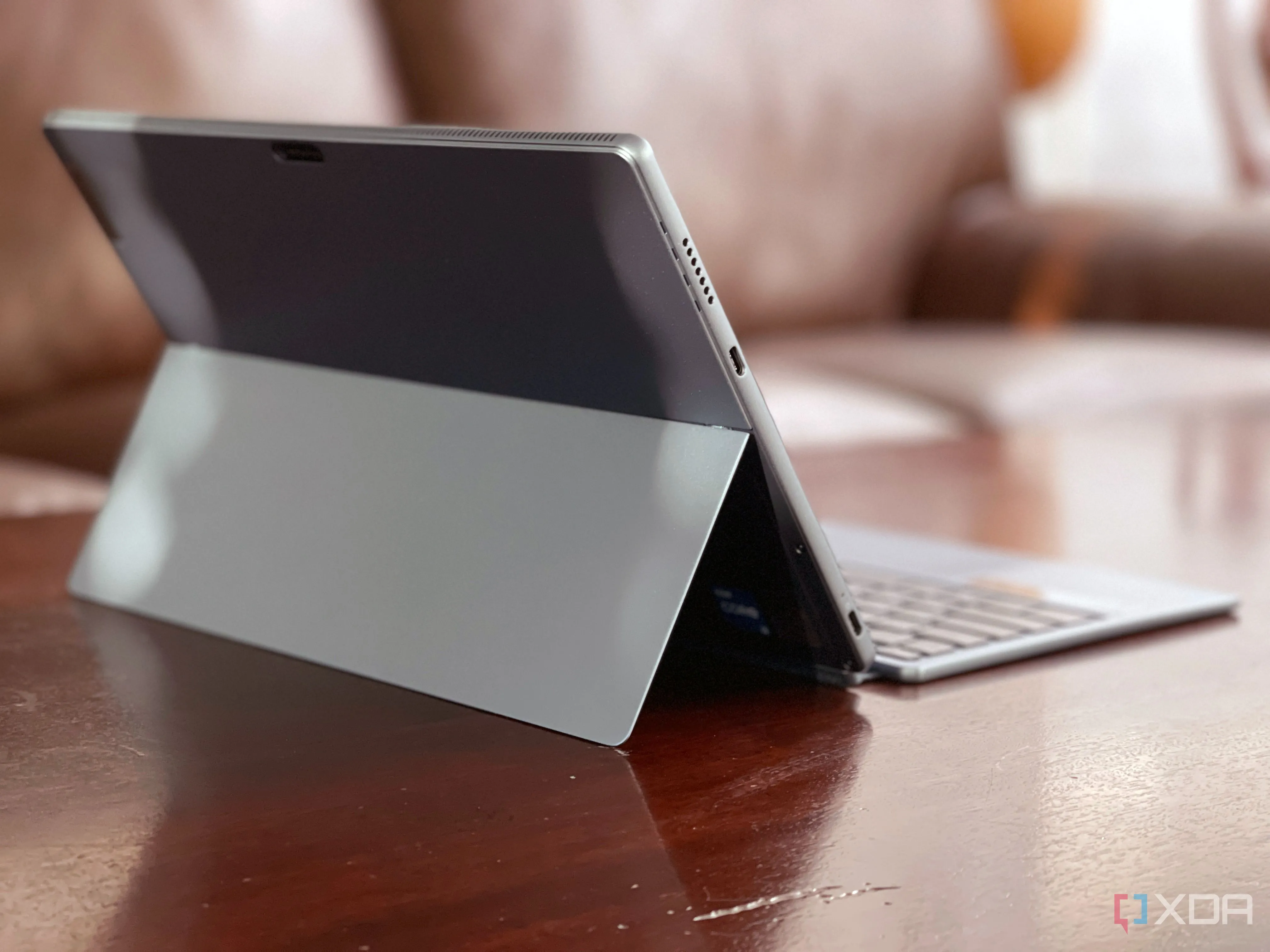 Lenovo IdeaPad Duet 5i màu xanh Abyss Blue nhìn từ phía sau, đặt trên bàn với ghế sofa làm nền, thể hiện tính năng 2-in-1