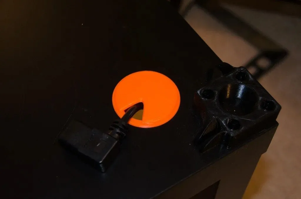 Vòng đệm luồn cáp in 3D màu xám với một sợi cáp đen chạy xuyên qua, giúp bàn làm việc gọn gàng
